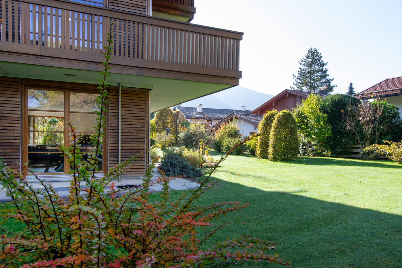 Garten und Terrasse der Mietwohnung im Landhaus Wallbergblick in Rottach-Egern mit gepflegtem Rasen, Sträuchern und Blick auf die Berge