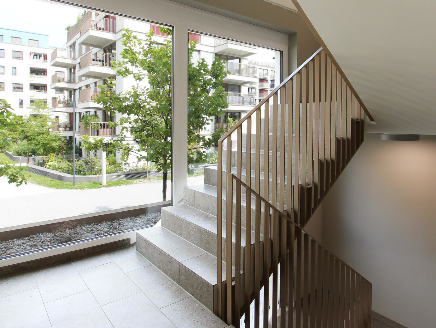 Treppenhaus im Haus D des Neubauquartiers kupa in München-Pasing mit großem Fenster und Blick auf die umliegenden Wohngebäude