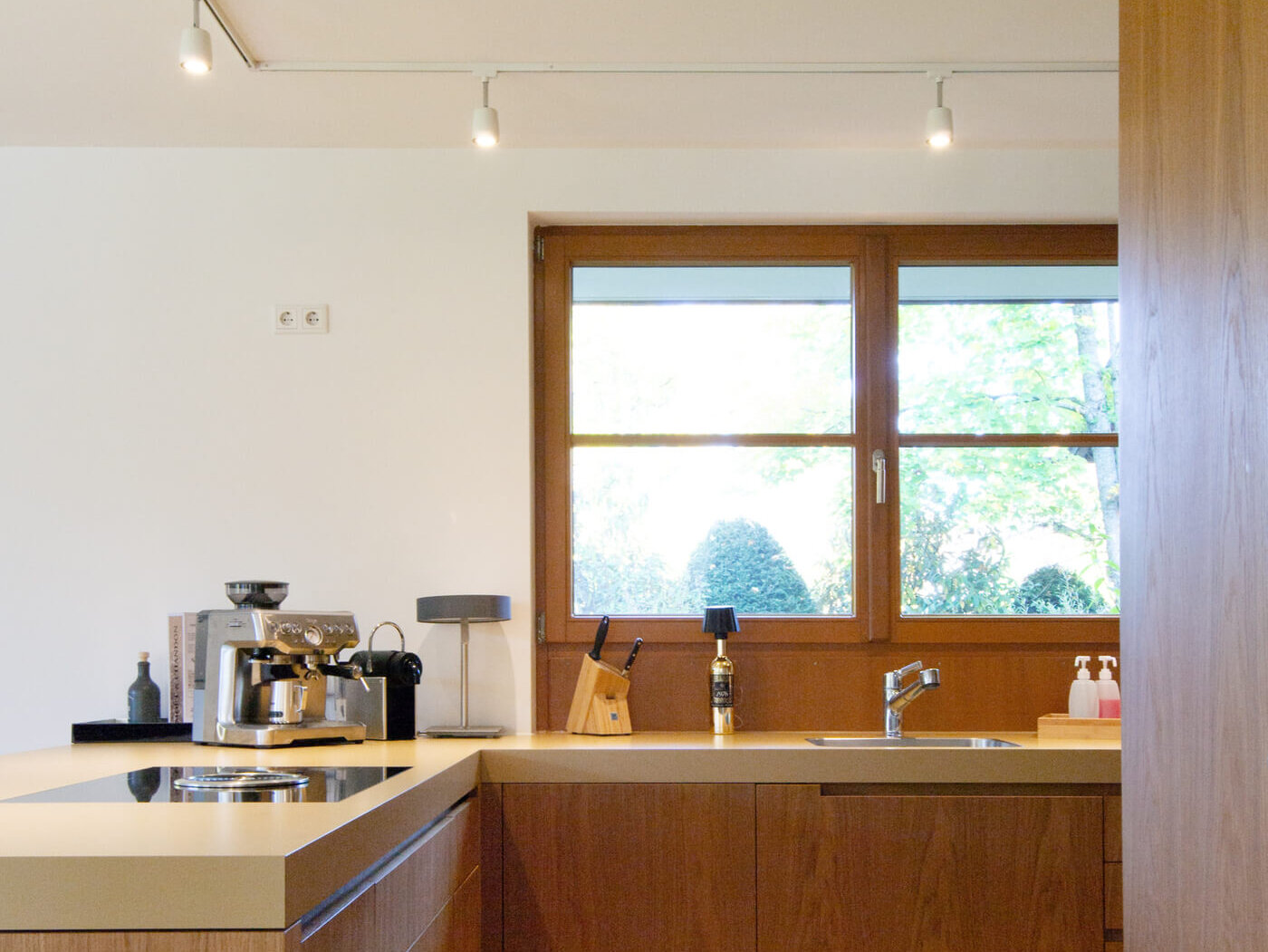 Moderne Küche der Mietwohnung 02 im Landhaus Wallbergblick in Rottach-Egern mit Holzfronten, Arbeitsfläche und Fenster mit Gartenblick