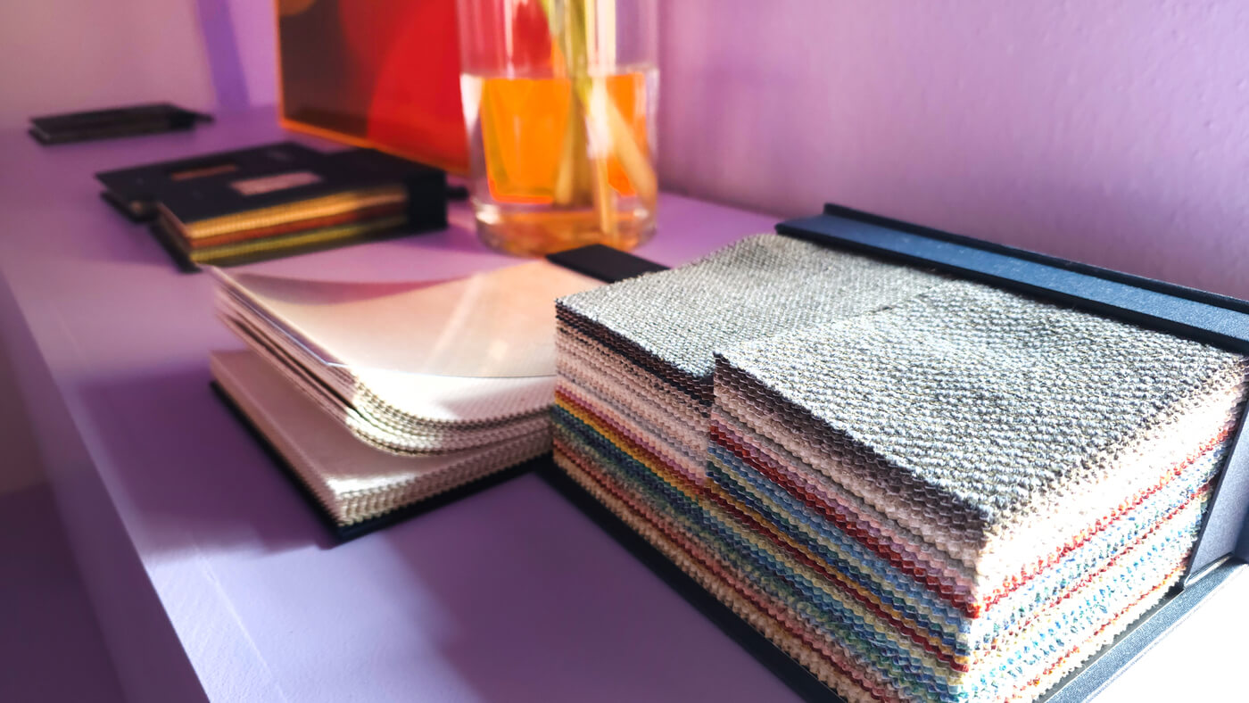 Gestapelte Stoffmuster und Bücher auf einer lila Oberfläche