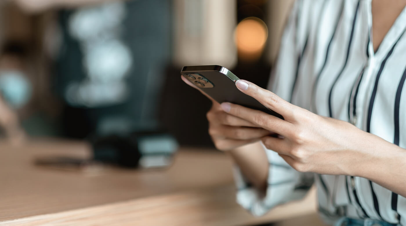 Person mit gestreifter Bluse hält Smartphone, unscharfe Küche im Hintergrund