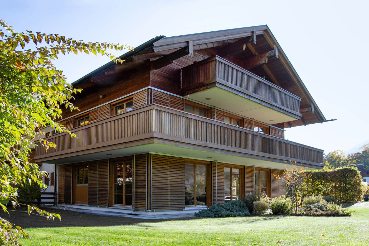 Fassadenansicht des Landhaus Wallbergblick in Rottach-Egern mit Holzverkleidung, großzügigen Balkonen und angrenzender Gartenfläche
