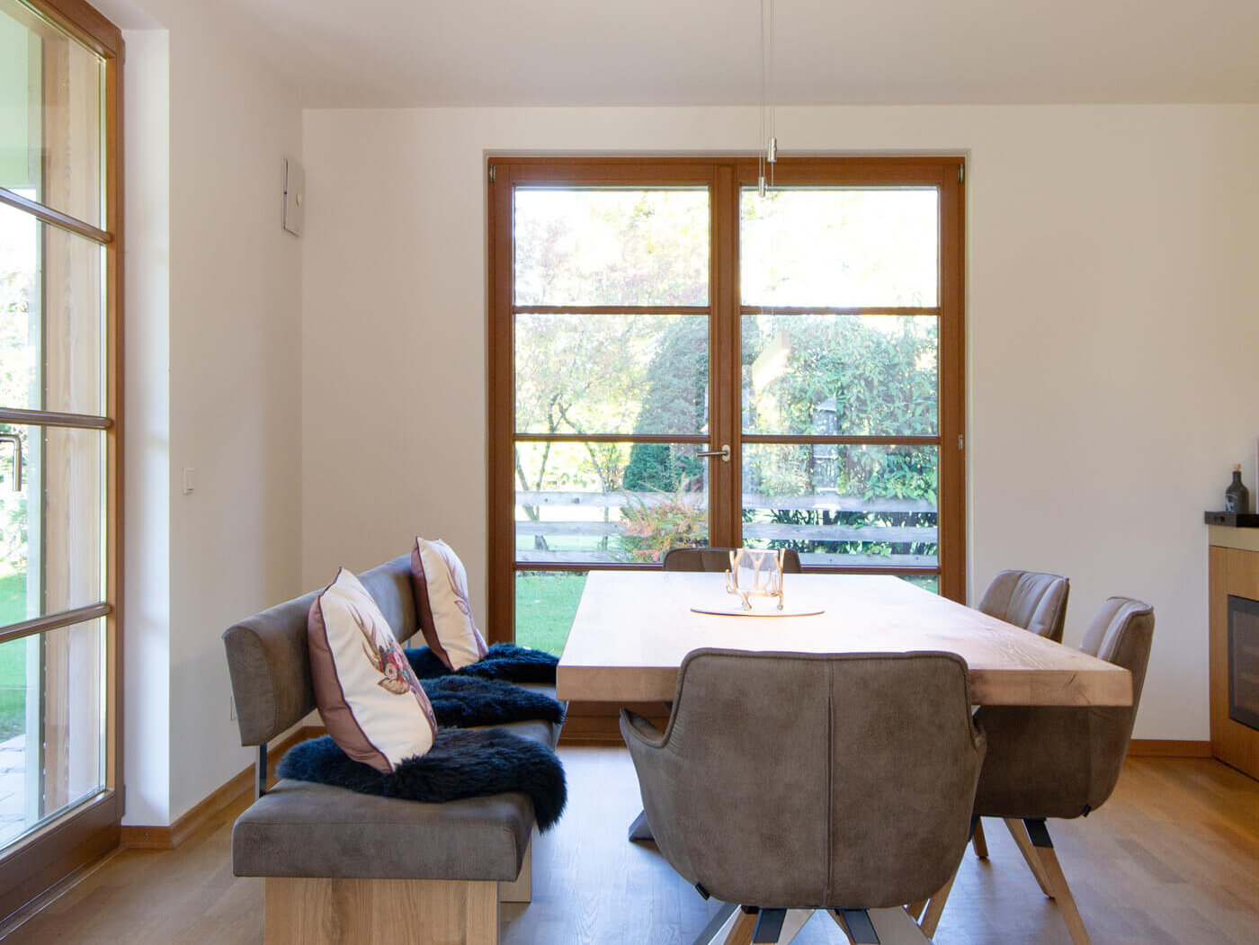 Essbereich der Mietwohnung 02 im Landhaus Wallbergblick in Rottach-Egern mit großem Holztisch, Stühlen und Blick in den grünen Garten