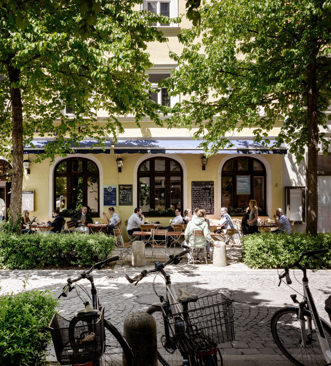 Café mit Außenplätzen und Fahrrädern vor Bäumen in München