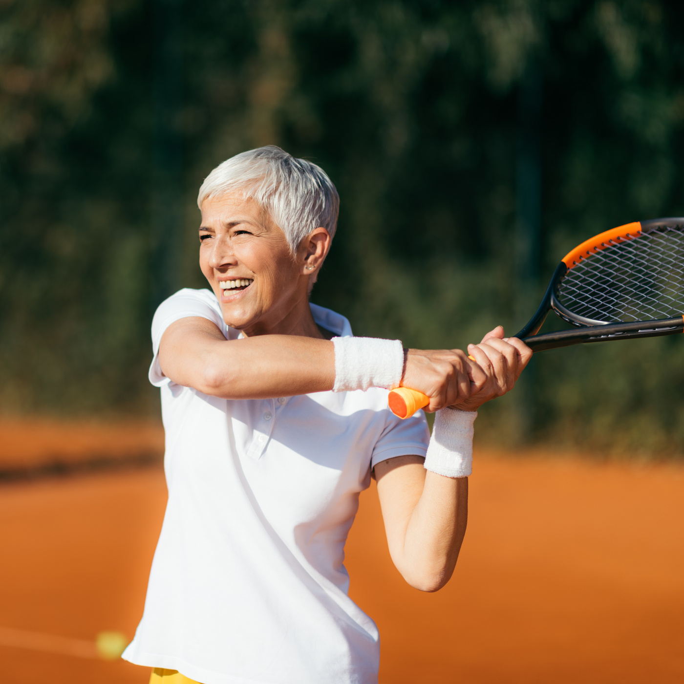Ältere Frau beim Tennisspielen auf einem Sandplat