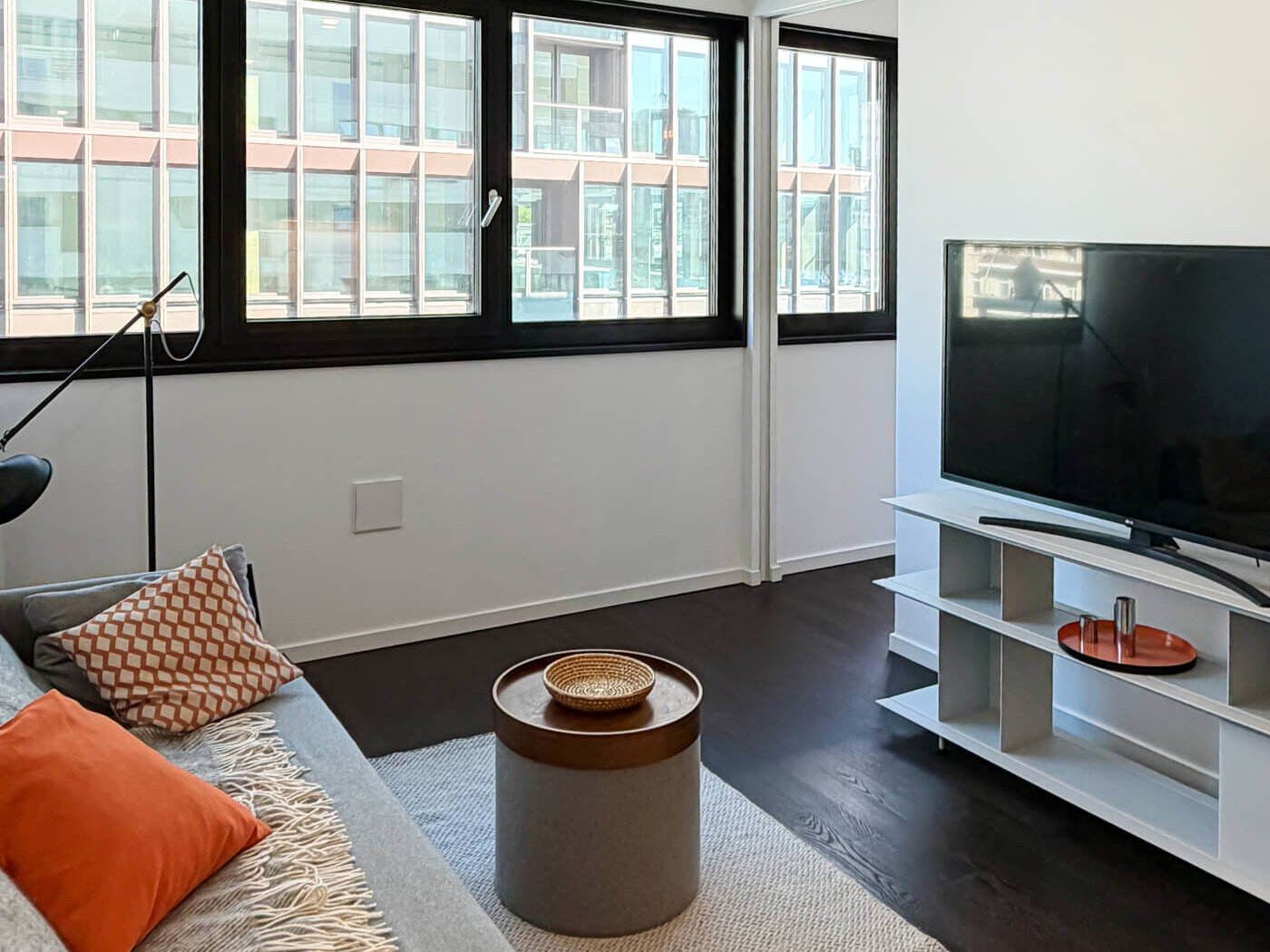 Wohnraum mit Sofa, TV und großem Fenster in Wohnung E.38 im Neubau WAVE Berlin
