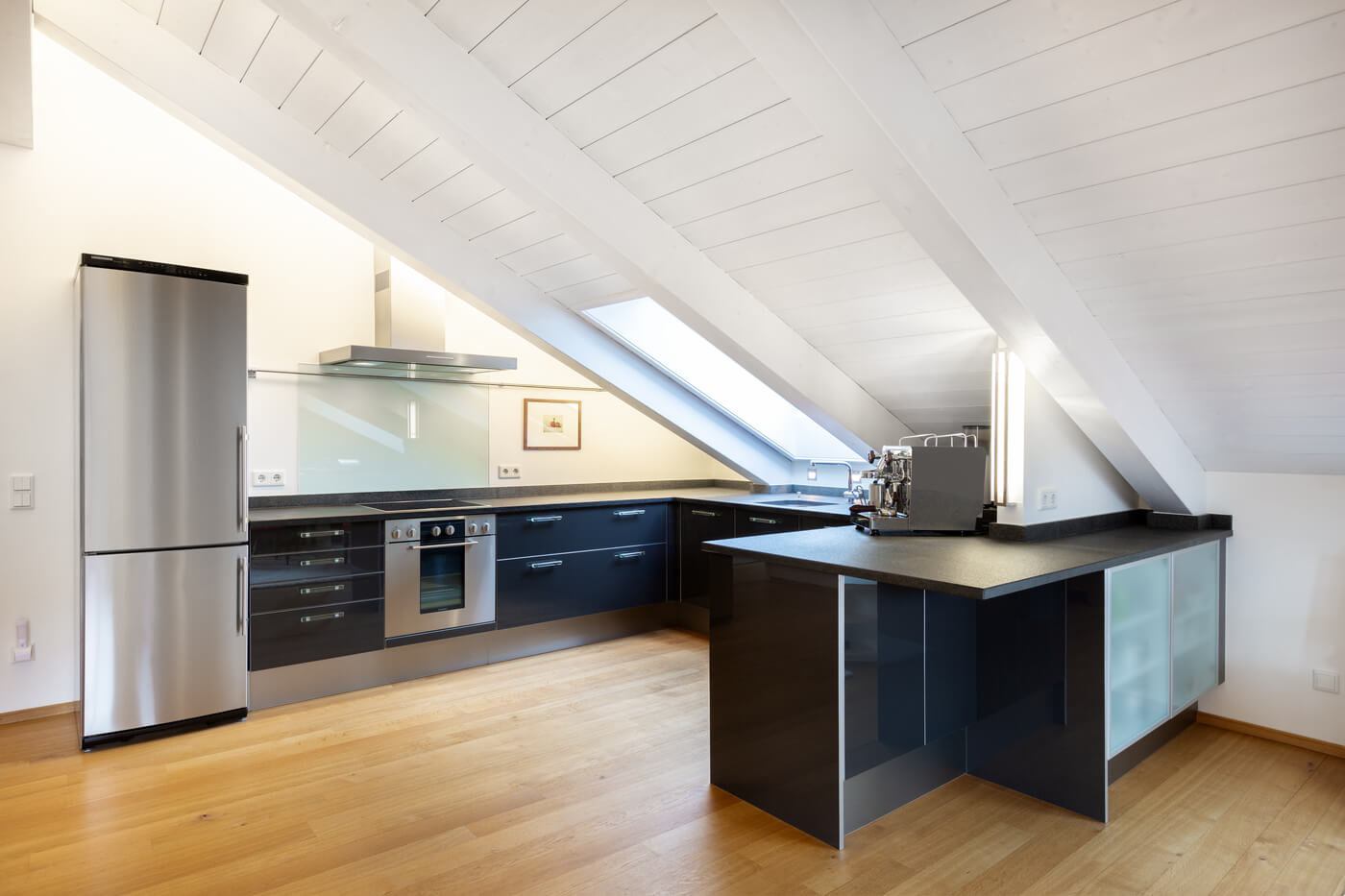 Moderne Einbauküche in der Dachgeschosswohnung des Landhauses Wallbergblick in Rottach-Egern mit dunklen Fronten, Kochinsel und Dachschrägenfenstern